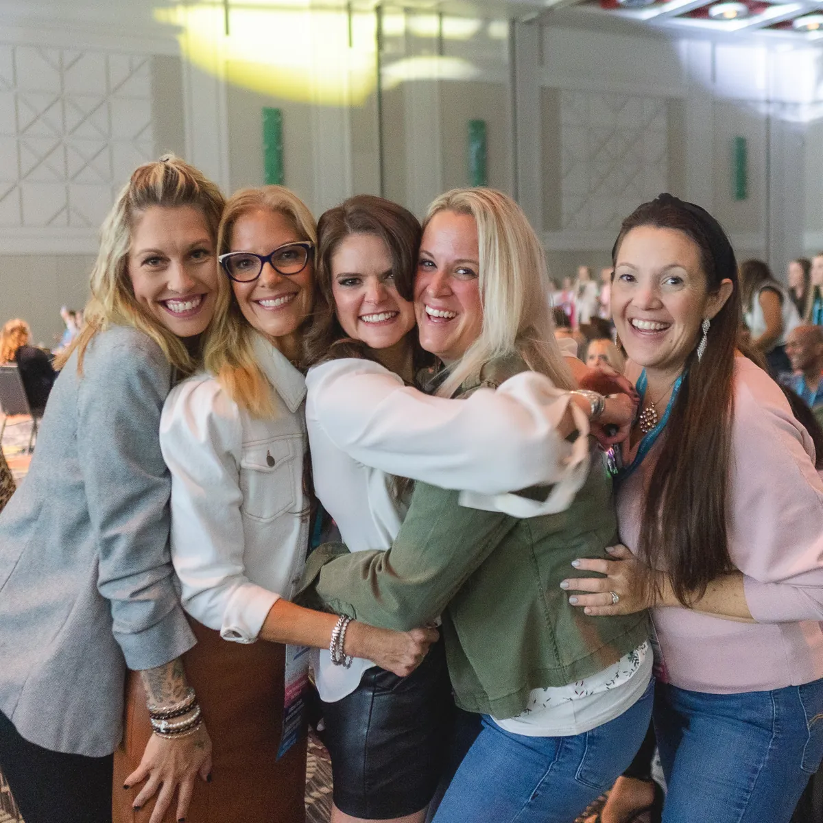 Lindsey Elmore in a group hug with four other women, all laughing, at an Amare convention