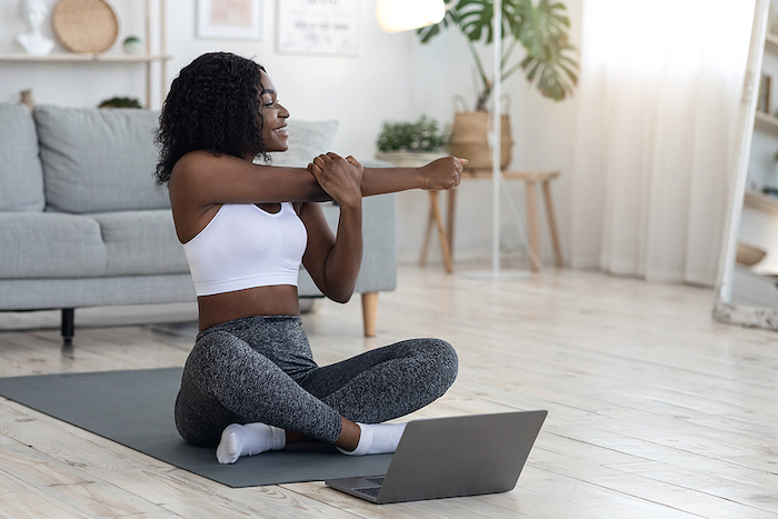 Fitness Online Concept. Athletic Black Woman Stretching At Living Room, Sitting On Yoga Mat In Front